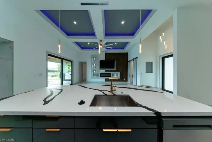 Kitchen with open floor plan, coffered ceiling, dishwashing machine, light stone counters, and pendant lighting