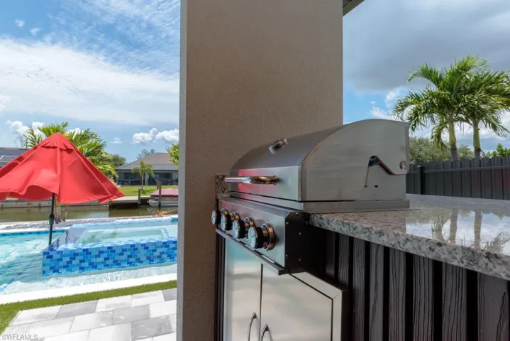 View of patio featuring area for grilling, a pool with connected hot tub, and an outdoor bar