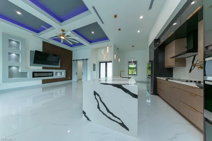 Kitchen featuring modern cabinets, coffered ceiling, open floor plan, light stone countertops, and a large island with sink