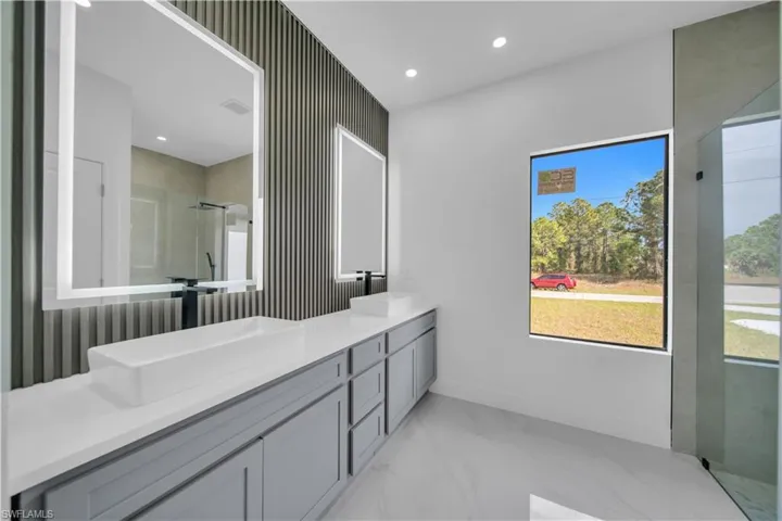 Full bath featuring a stall shower, double vanity, recessed lighting, and light marble finish flooring