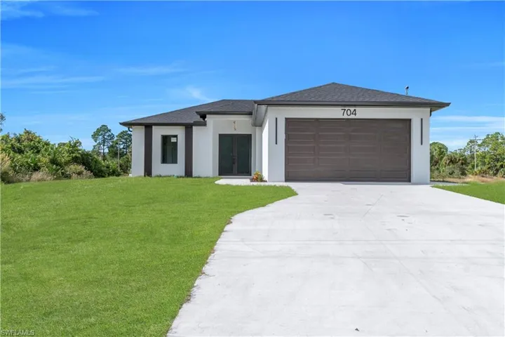 View of front of property featuring a front yard, french doors, concrete driveway, a garage, and stucco siding