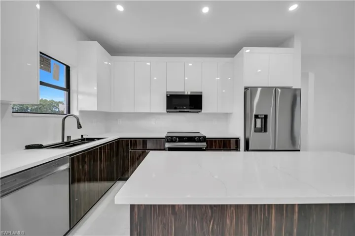 Kitchen with modern cabinets, stainless steel appliances, light stone countertops, a kitchen island, and recessed lighting