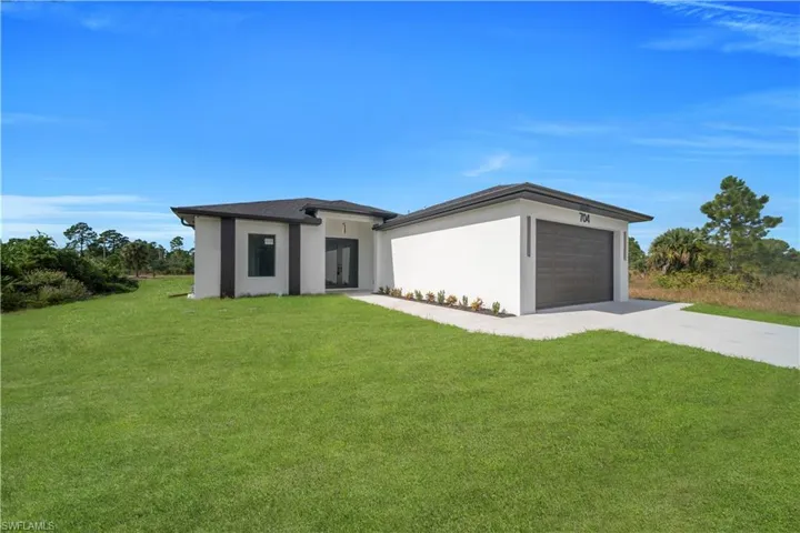 View of front facade with a front yard, driveway, stucco siding, and an attached garage