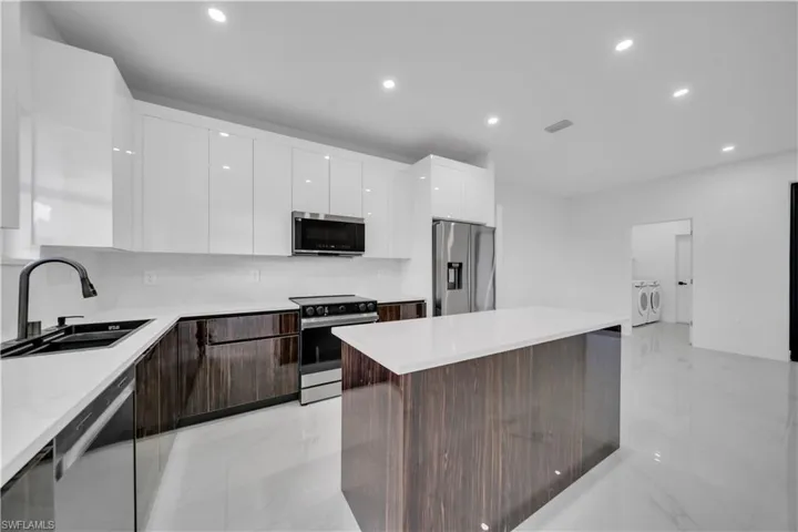 Kitchen featuring modern cabinets, stainless steel appliances, two tone color scheme, recessed lighting, and a kitchen island