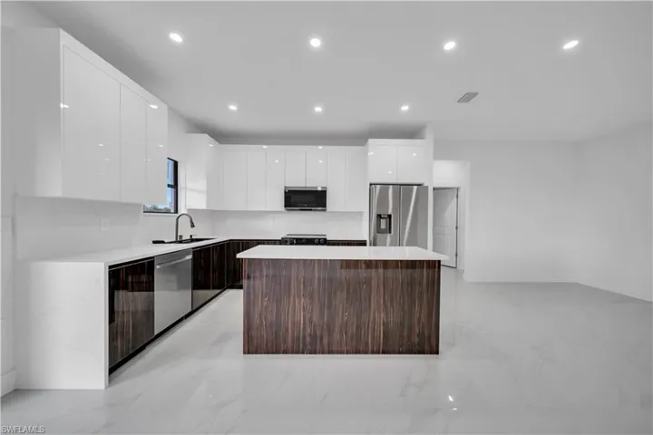 Two tone kitchen featuring modern cabinets, stainless steel appliances, a kitchen island, two tone cabinets, and recessed lighting