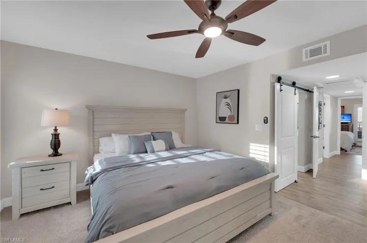 Bedroom with a barn door, a ceiling fan, and light carpet