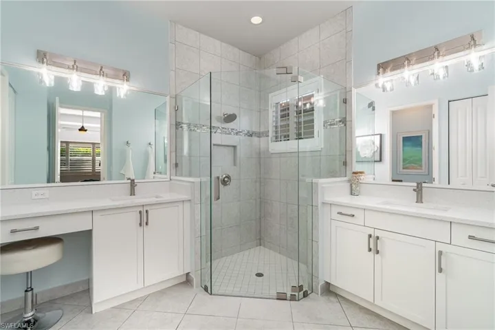 Primary bathroom with frameless glass walk-in shower, recessed shower shelf, dual sinks, vanity sitting area, plantation shutters, linen closet, and water closet with pocket door.