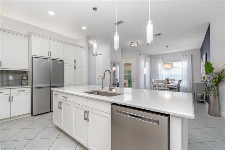 Kitchen with stainless steel appliances, island with sink, and decorative pendant lights.