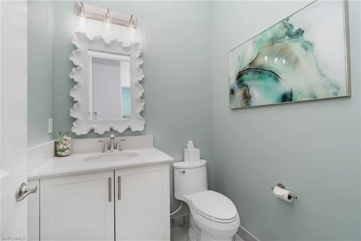 Guest half bathroom featuring vanity with quartz counter, framed mirror, and new toilet.