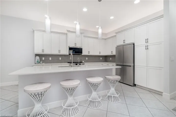 Kitchen with stainless steel appliances, light tile flooring, quartz countertops, tile backsplash, and seating for four.