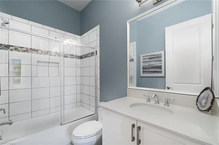 Guest bathroom featuring shower / bath combination with glass door, recessed shower shelf, new toilet, framed mirror, and quartz counter.