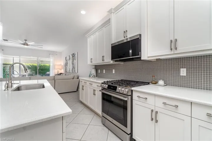 Open kitchen featuring stainless steel appliances, light tile flooring, tile backsplash, quartz counters and white cabinetry.