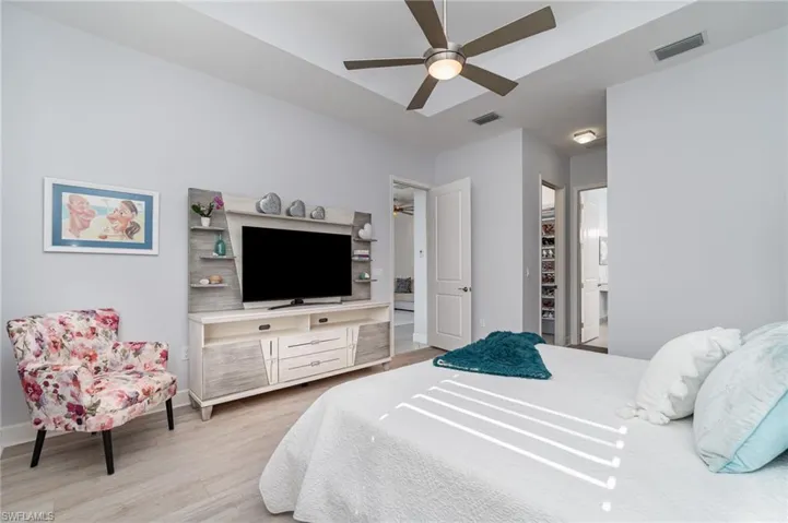 Primary bedroom with LVT flooring, two walk-in closets, ensuite bathroom, and a ceiling fan.