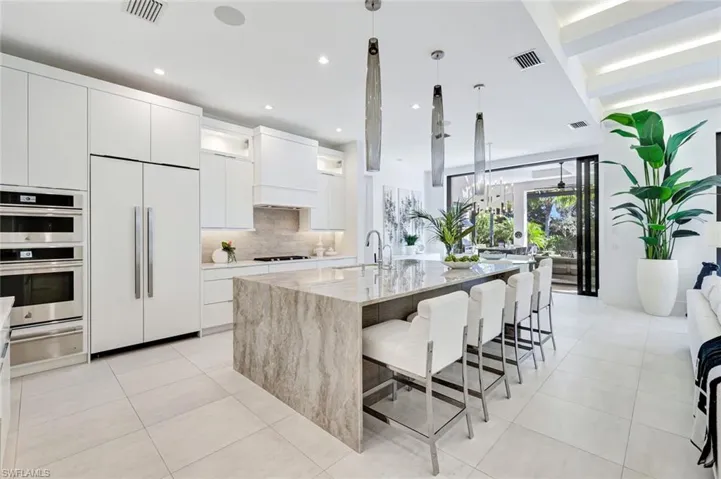 Kitchen with white cabinetry, modern cabinets, paneled built in refrigerator, decorative light fixtures, and light stone counters