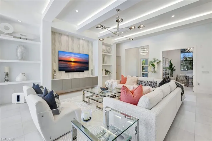 Living room featuring built in shelves, light tile patterned flooring, beam ceiling, a chandelier, and recessed lighting