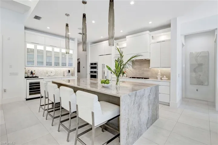 Kitchen with glass insert cabinets, white cabinets, a kitchen breakfast bar, light stone counters, and hanging light fixtures