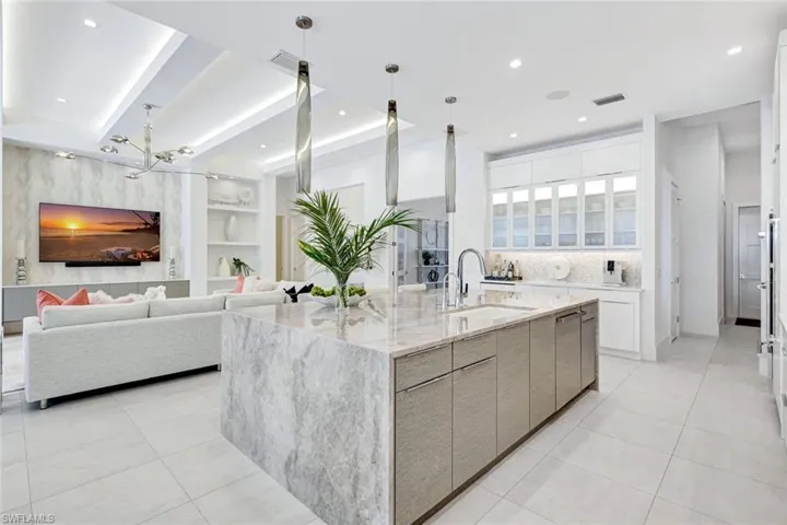 Kitchen with built in features, an island with sink, light stone counters, beam ceiling, and recessed lighting