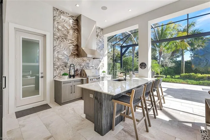 Kitchen featuring light stone counters, modern cabinets, a kitchen breakfast bar, wall chimney range hood, and a sunroom