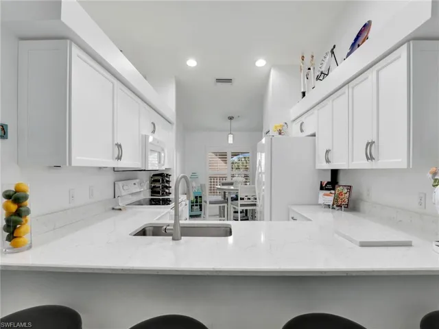 Kitchen with a kitchen breakfast bar, light stone countertops, white cabinetry, and white appliances