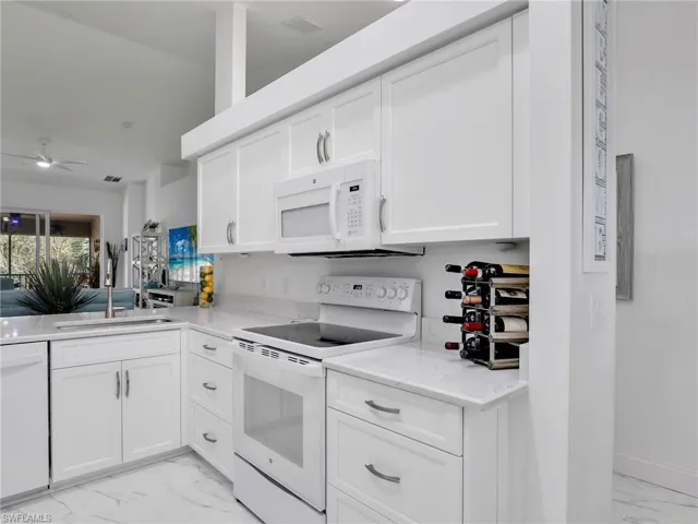 Kitchen with ceiling fan, white cabinets, sink, and white appliances