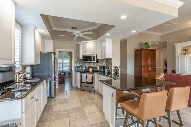 Kitchen with white cabinetry, sink, stainless steel appliances, crown molding, and a tray ceiling