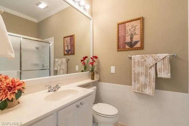 Bathroom featuring an enclosed shower, vanity, crown molding, tile walls, and toilet