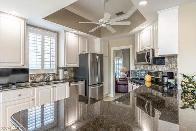 Kitchen with white cabinets, sink, appliances with stainless steel finishes, and a tray ceiling