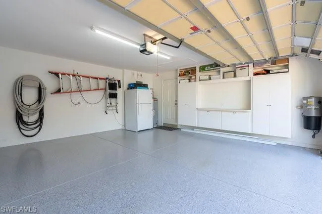 Garage with gas water heater, white fridge, and a garage door opener