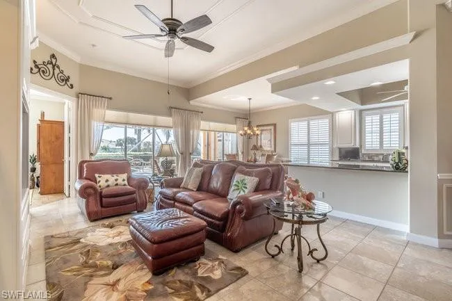 Living room with ceiling fan with notable chandelier, light tile patterned flooring, crown molding, and a wealth of natural light