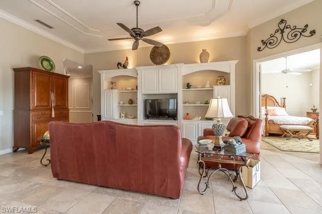 Living room with built in shelves, ceiling fan, and ornamental molding