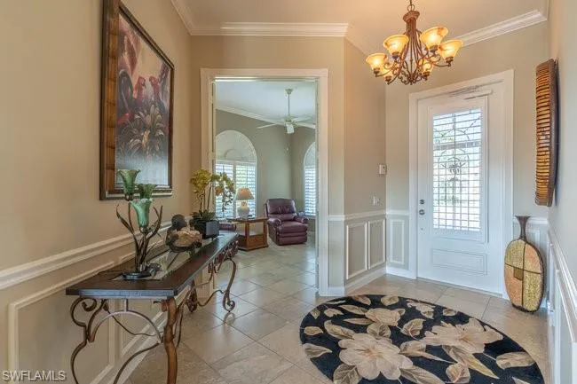 Entryway with crown molding, light tile patterned flooring, and ceiling fan with notable chandelier