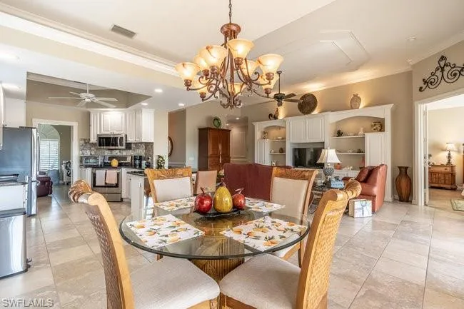 Tiled dining room with ceiling fan with notable chandelier and crown molding