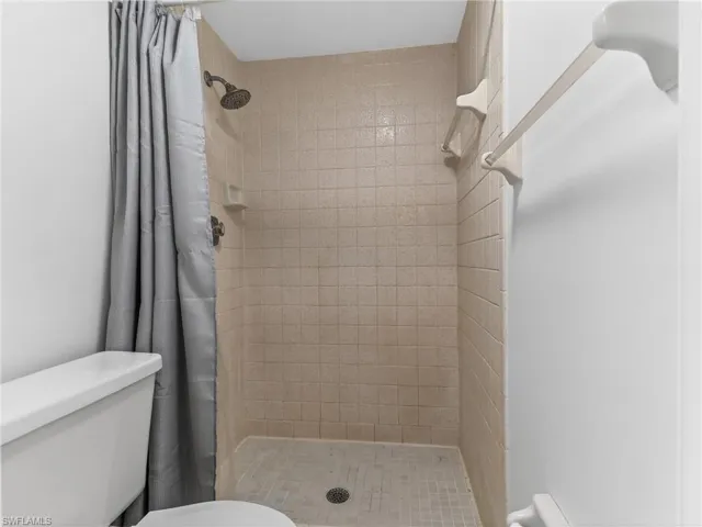 Shower stall featuring light-toned square wall tiles and a mosaic tile floor