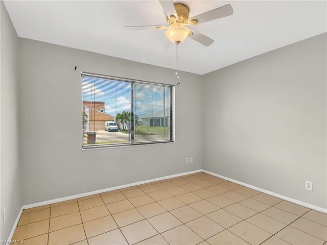 Spacious room featuring neutral painted walls, tiled flooring, a window with horizontal blinds, and a ceiling fan with integrated lighting