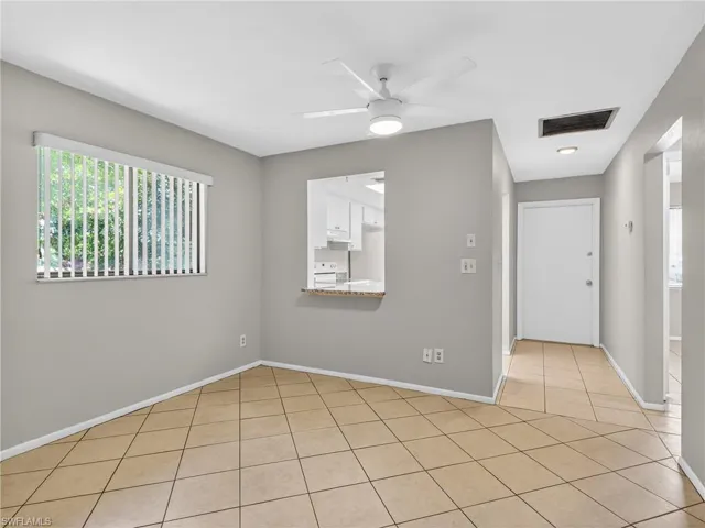 Tile flooring extending throughout, a pass-through window with a stone counter, a ceiling fan with integrated lighting, and a white entry door