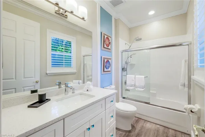 Full bath featuring vanity, enclosed tub / shower combo, ornamental molding, and light wood-type flooring