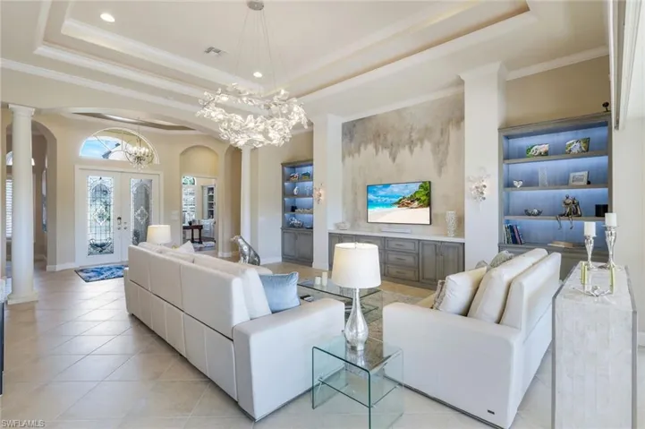 Living room featuring built in shelves, ornamental molding, arched walkways, a raised ceiling, and french doors