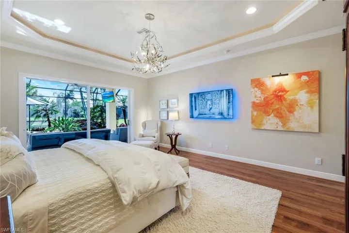 Bedroom featuring crown molding, a raised ceiling, dark wood-style floors, a chandelier, and access to outside