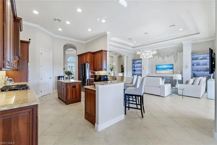 Kitchen featuring arched walkways, a breakfast bar, crown molding, open floor plan, and light stone countertops