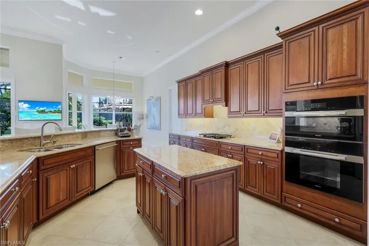 Kitchen featuring a chandelier, light stone counters, a center island, pendant lighting, and ornamental molding