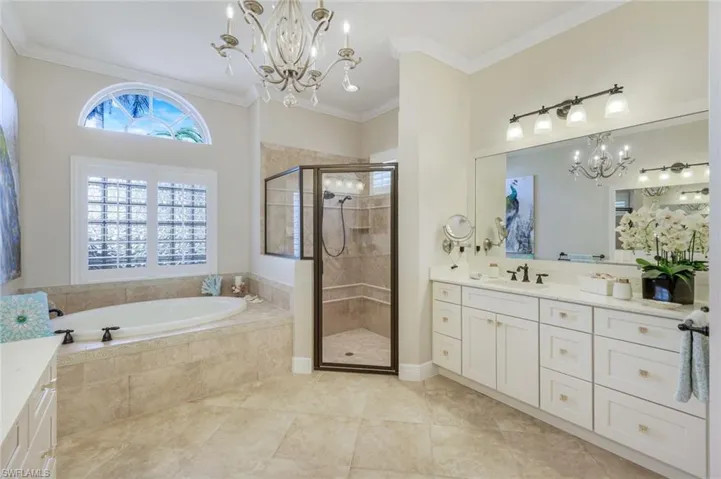Full bath featuring a chandelier, vanity, a garden tub, crown molding, and a shower stall