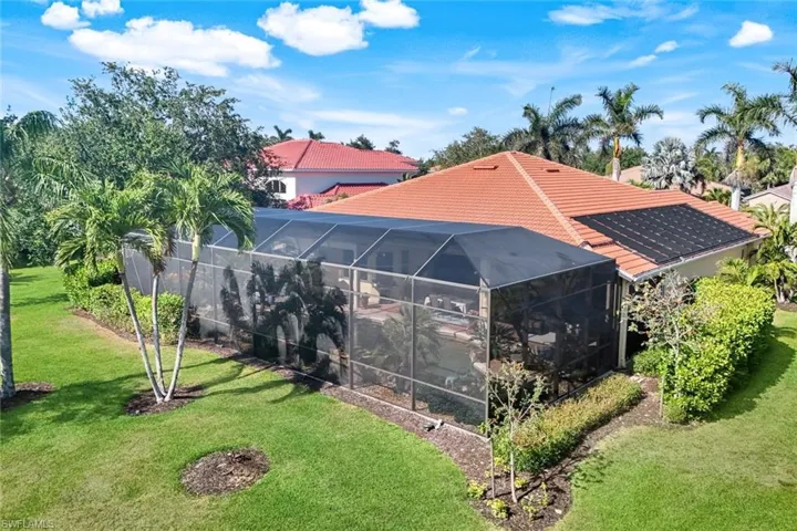 Back of house featuring a lawn, a lanai, and solar panels