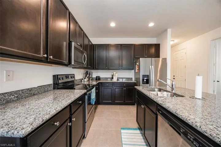 Kitchen with a sink, light stone countertops, stainless steel appliances, and light tile patterned flooring