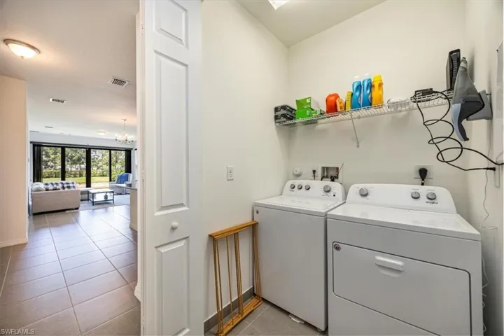 Laundry room with light tile patterned floors, visible vents, a notable chandelier, and washing machine and clothes dryer