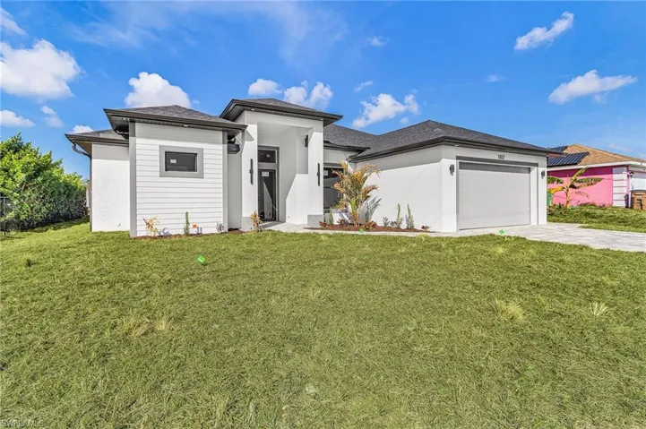 Prairie-style home featuring a front yard, an attached garage, driveway, and stucco siding