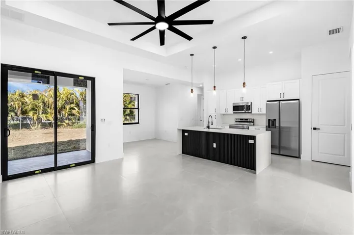 Kitchen featuring decorative light fixtures, stainless steel appliances, an island with sink, white cabinets, and open floor plan