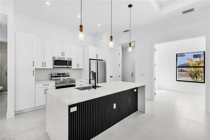 Kitchen with stainless steel appliances, hanging light fixtures, light stone countertops, white cabinets, and a high ceiling