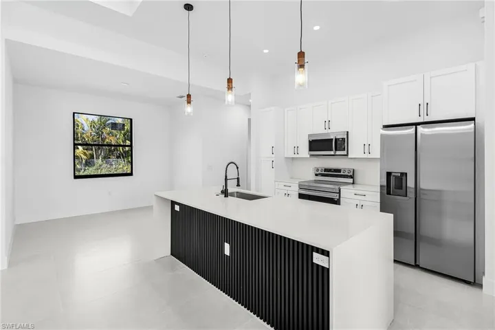 Kitchen with stainless steel appliances, pendant lighting, white cabinetry, and light stone counters