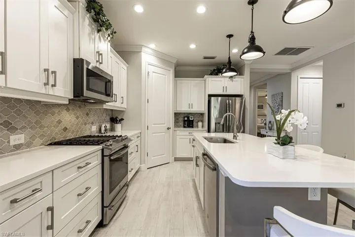 Kitchen featuring stainless steel appliances, a breakfast bar, pendant lighting, white cabinetry, and light wood finished floors