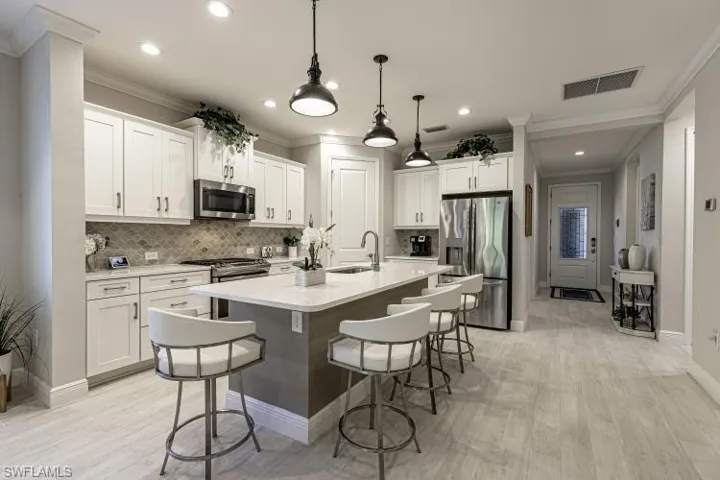 Kitchen with stainless steel appliances, a breakfast bar, decorative light fixtures, white cabinets, and ornamental molding